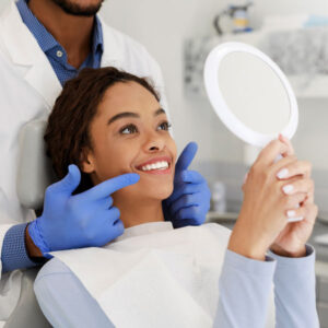 young woman looking at smile in mirror after getting Dental Implants in Burnsville, Apple Valley, Eagan, Savage, MN, Lakeville, MN, Owatonna