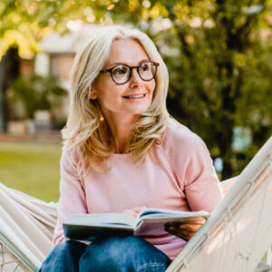 mature woman in glasses reading book outside in hammock after receiving Dental Surgery in Apple Valley, Savage, MN, Burnsville, Lakeville, MN, Owatonna, and Shakopee